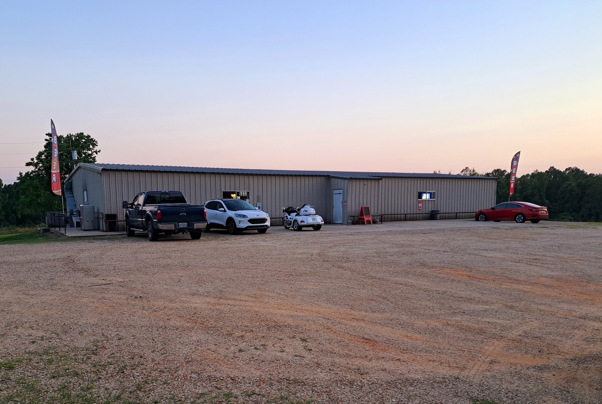 Big's Place at twilight — the long metal building behind its gravel lot with trucks parked outside