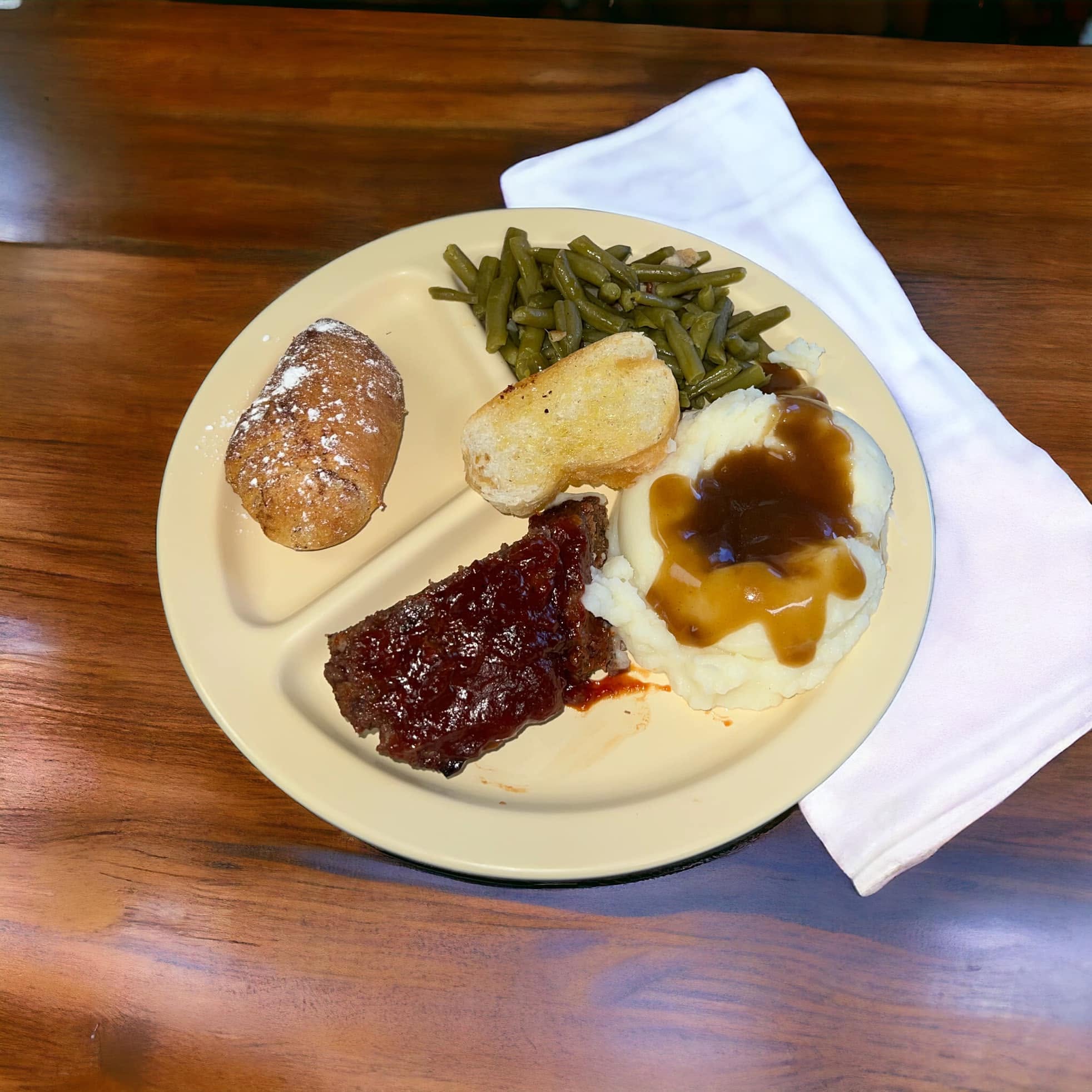 A divided plate of meat with gravy, mashed potatoes, green beans and a roll