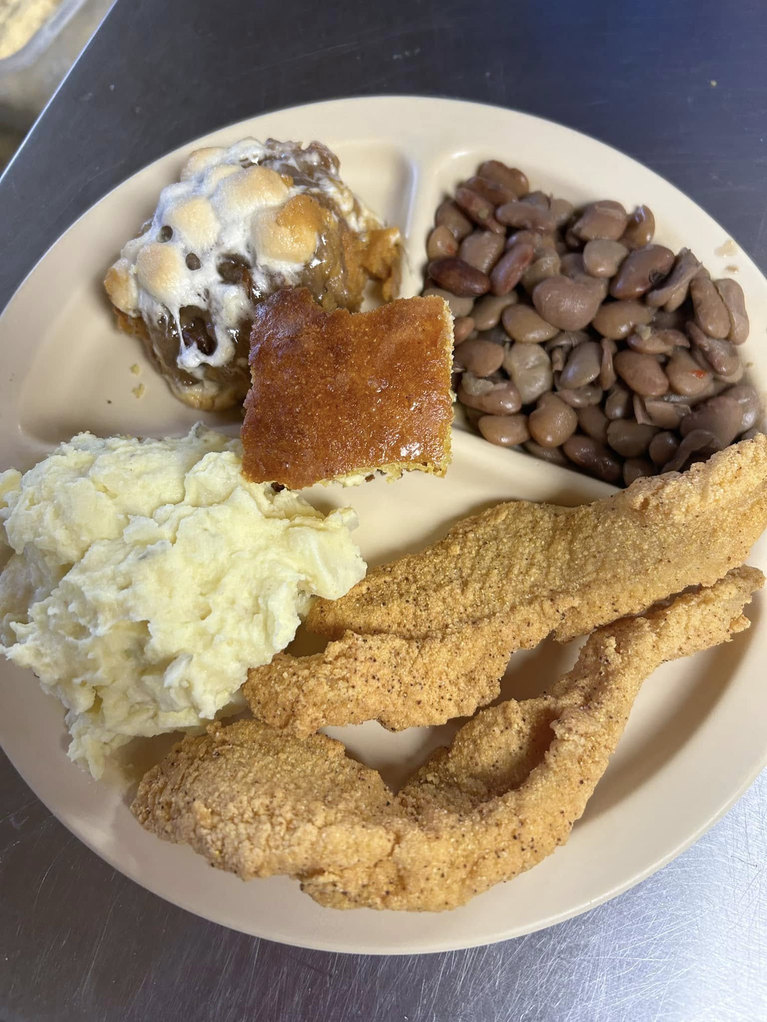 A plate of fried fish fillets with mashed potatoes, baked beans and cornbread