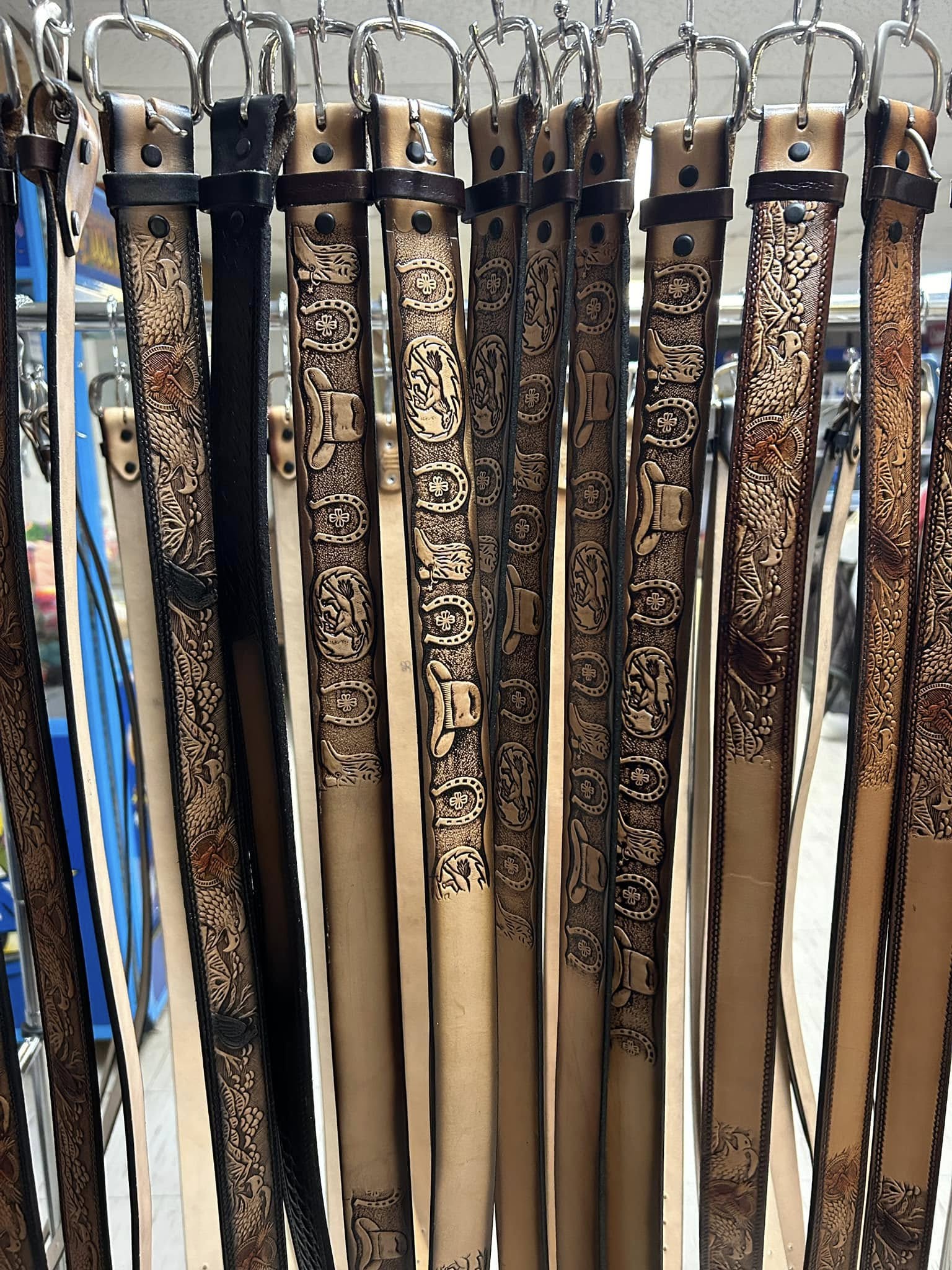 Tooled leather belts hanging from hooks — floral and western patterns from tan to black